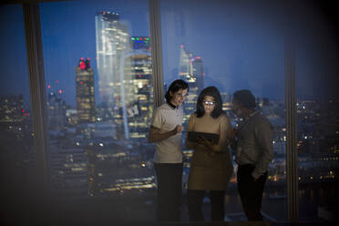 Geschäftsleute mit digitalem Tablet arbeiten bis spät in die Nacht am Fenster eines Hochhauses - CAIF29717