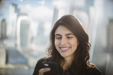 Smiling businesswoman using smart phone in sunny window - CAIF29736