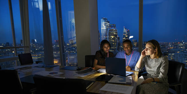 Business people working late at laptop in highrise conference room - CAIF29746