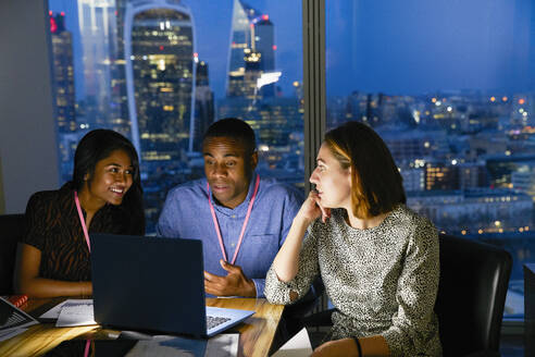 Business people working late at laptop in urban highrise office - CAIF29750