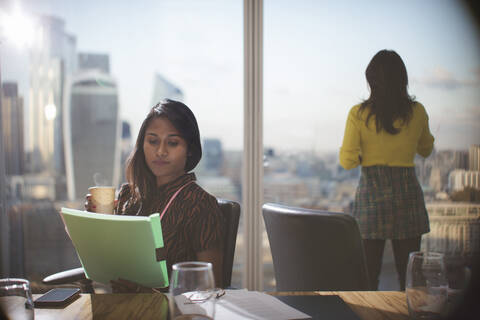 Businesswoman with coffee reviewing paperwork in conference room stock photo