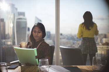 Businesswoman with coffee reviewing paperwork in conference room - CAIF29761