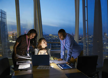 Business people working late at laptop in highrise conference room - CAIF29767