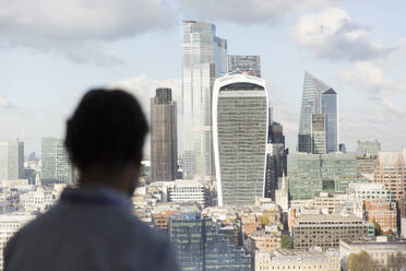 Businessman looking at sunny London cityscape from office window, UK - CAIF29782