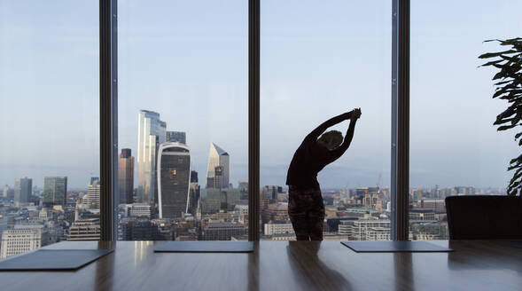 Geschäftsfrau streckt sich am Fenster eines Hochhausbüros, London, UK - CAIF29792
