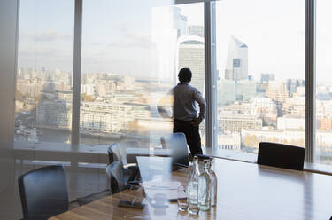 Nachdenklicher Geschäftsmann am Fenster eines Hochhausbüros, London, UK - CAIF29798