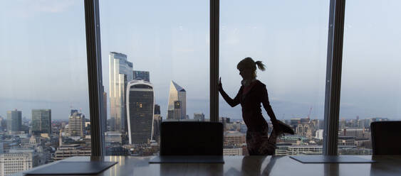 Businesswoman stretching at highrise office window, London, UK - CAIF29808