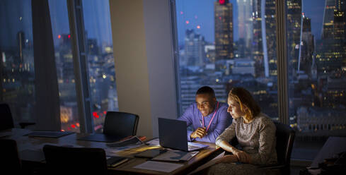 Geschäftsleute arbeiten bis spät in die Nacht am Laptop in einem Hochhausbüro, London, UK - CAIF29816