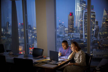 Geschäftsleute arbeiten bis spät in die Nacht am Laptop in einem Hochhausbüro, London, UK - CAIF29819