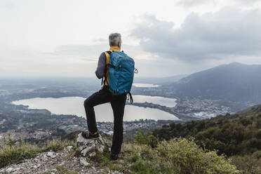 Älterer männlicher Tourist mit Rucksack schaut auf den See und die Stadt gegen den Himmel bei Sonnenuntergang - MCVF00634