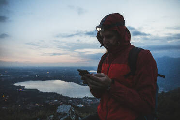 Älterer Mann benutzt Mobiltelefon gegen den Himmel in der Dämmerung - MCVF00636