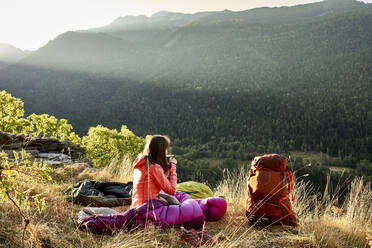 Woman looking at view while drinking coffee sitting in forest - VEGF03015