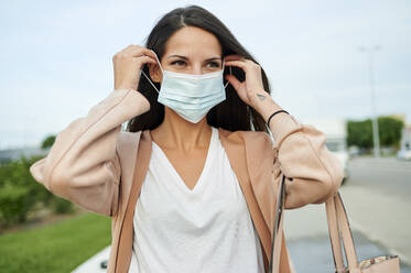 Young woman looking away while wearing protective face mask standing on street - KIJF03358