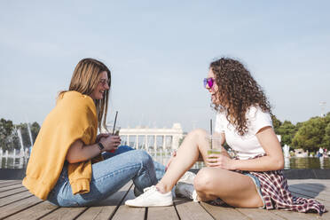 Cheerful friends enjoying weekend while talking at park against sky on sunny day - VYF00150