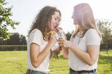 Glückliche Freundinnen teilen sich an einem sonnigen Tag Limonaden im Park - VYF00155