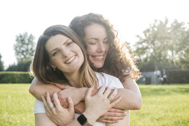 Beautiful woman being hugged from smiling young female friend at park - VYF00159