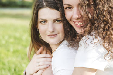 Happy young woman hugging beautiful female friend from behind at park - VYF00160