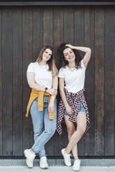 Happy beautiful women leaning against brown wooden wall - VYF00180