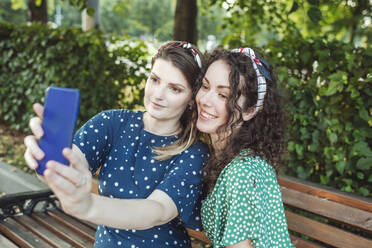 Schöne Frau nimmt Selfie mit jungen weiblichen Freund sitzen im Park - VYF00190