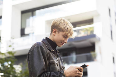 Blonder Teenager mit Smartphone in der Stadt - SGF02699