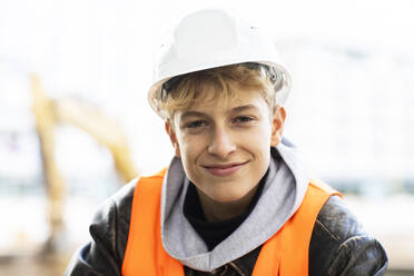 Lächelnder männlicher Auszubildender im Baugewerbe mit Schutzhelm auf der Baustelle - SGF02706