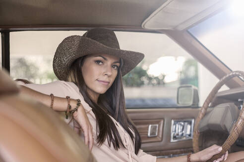 Confident woman wearing hat sitting in car - AJOF00375