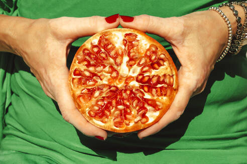 Hands of woman holding halved pomegranate - ERRF04649