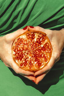 Hands of woman holding halved pomegranate - ERRF04650