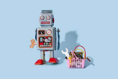 Studio shot of vintage robot toy standing by miniature shopping basket filled with electronic equipment - GEMF04266