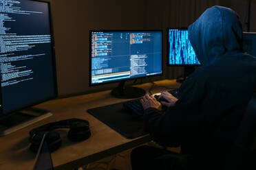 Hacker mit Kapuzenpulli bei der Arbeit am Computer, während er im Büro sitzt - JRFF04779
