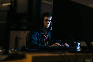 Junger Hacker, der am Computer arbeitet, während er im Büro sitzt - JRFF04782