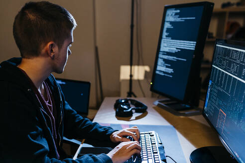 Männlicher Hacker, der auf einen Computer schaut, während er im Büro arbeitet - JRFF04785