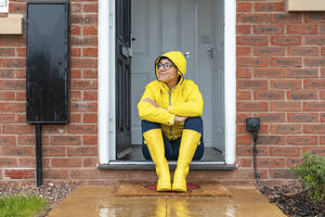 Frau schaut weg, während sie in der Regenzeit zu Hause auf der Tür sitzt - WPEF03472