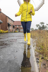 Woman running in puddle on street during rainy season - WPEF03480