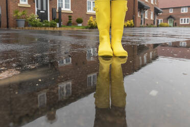 Close-up of woman standing in water puddle during rainy season - WPEF03482