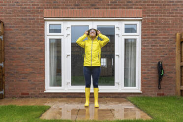 Frau im Regenmantel schaut nach oben, während sie in einem Hinterhof während der Regenzeit steht - WPEF03484