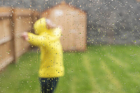 Frau genießt den Regen mit ausgestreckten Armen, während sie in einem Hinterhof während der Regenzeit steht - WPEF03489