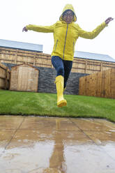 Cheerful woman jumping in back yard during rainy season - WPEF03491