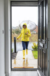 Frau läuft mit Regenschirm zu Hause während der Regenzeit - WPEF03493