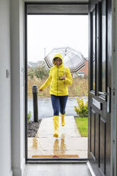 Woman running with umbrella at home during rainy season - WPEF03493