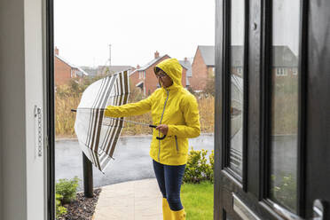 Mittlere erwachsene Frau, die ihren Regenschirm schließt, bevor sie nach Hause geht - WPEF03494