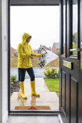 Woman closing umbrella standing in back yard before going at home - WPEF03495
