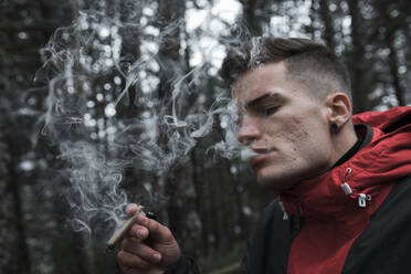 Junger Mann, der im Herbst im Wald steht und Zigarette raucht - ACPF00866