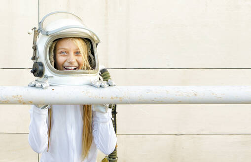 Girl wearing space suit leaning on railing against wall during sunny day - GGGF00005