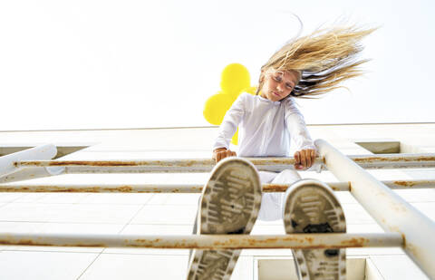 Low angle view of girl standing on railing with tousled hair during sunny day stock photo