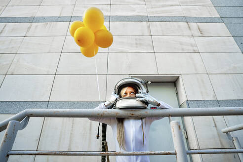 Girl leaning on railing while holding yellow balloon - GGGF00008