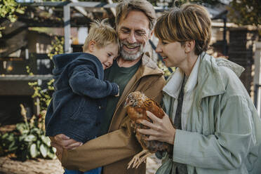 Smiling family with chicken coop standing in back yard - MFF06617