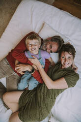 Mutter, Vater und Sohn umarmen sich gegenseitig, während sie zu Hause auf dem Bett liegen - MFF06633