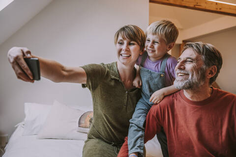 Glückliche Mutter nimmt Selfie auf Smartphone, während Vater und Sohn sitzen neben zu Hause, lizenzfreies Stockfoto