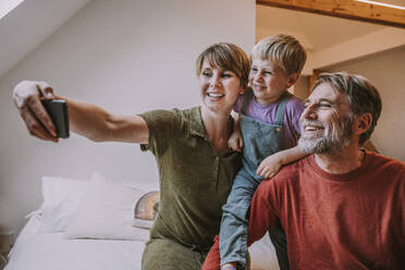 Glückliche Mutter nimmt Selfie auf Smartphone, während Vater und Sohn sitzen neben zu Hause - MFF06648